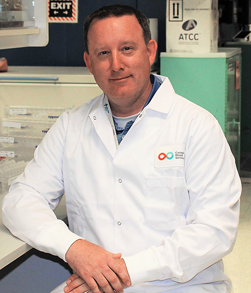 Jason Acker, PhD (above), Senior Research Scientist, Canadian Blood Services, and Professor of Laboratory Medicine and Pathology at the University of Alberta in a white lab jacket in a laboratory